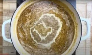 Simmering curry in a white pot on a wooden table. Bubbles and rich spices create a swirling pattern on the surface.